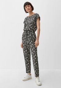 Combinaison à imprimé animal noir et blanc avec manches courtes, taille élastique et jambes fuselées, assortie à des sneakers à plateforme blanches. Tissu lisse.