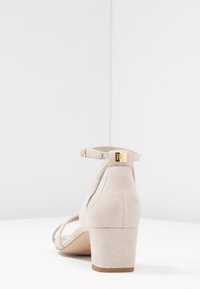 Bežové semišové sandály na blokovém podpatku pro ženy s náramkem na kotníku a zlatou sponou se značkou "RL", vystavené na bílém povrchu a pozadí.