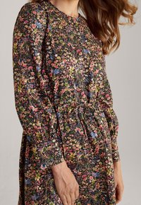 Vestido de estampado floral con mangas largas abullonadas, cintura ceñida y fondo negro. Presenta pequeñas flores multicolores por toda la prenda.