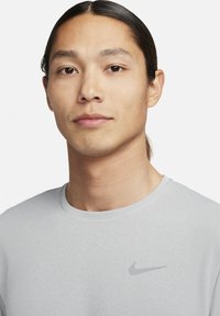 Harmaa pyöreäkauluksinen t-paita, joka on valmistettu pehmeästä kankaasta. Paita on koristeltu hienovaraisella Nike-logolla, joka on hieman tummempaa harmaata vasemmassa rinnassa.