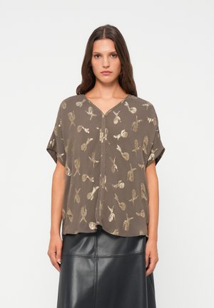 Brun kortermet bluse med V-hals, med gull paisley-mønster og løs passform, kombinert med et svart skinnskjørt.