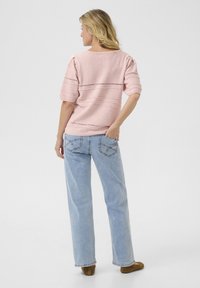 Svetlo roza teksturiran pulover s kratkimi rokavi, ki ima vodoravne črte in izrezane detajle, v kombinaciji s svetlo modrimi ravnimi hlačami.