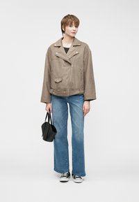 Taupe faux suede jakke med sølv detaljer, frontlommer, belte, kombinert med utslåtte blå jeans og svarte sko, bærende på en svart veske.