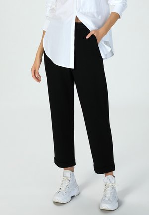 Schwarze Jogginghosen mit umgeschlagenen Bündchen, aus weichem Material. Kombiniert mit einem weißen Hemd und weißen High-Top-Sneakern. Einfaches Design, keine sichtbaren Muster.