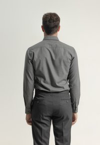 Camisa gris de manga larga con una textura suave, puños abotonados y un cuello suave, combinada con pantalones oscuros grises ajustados que tienen bolsillos traseros.
