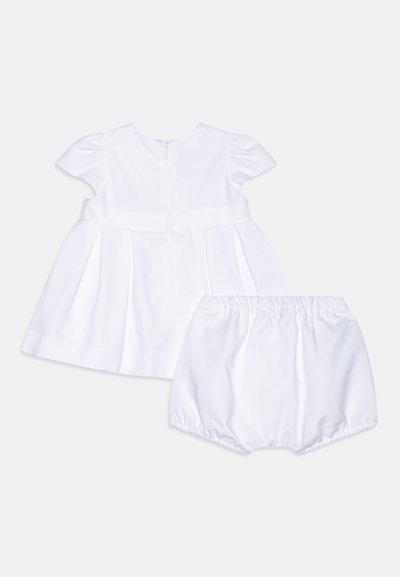 Hvit kjole med korte pufferm og en plisserte skjørt, sammen med matchende hvite bloomers. Glidelås lukking bak. Tekstuert stoff.