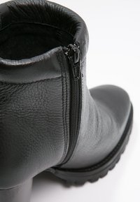 Botte de cheville en cuir noir avec une finition texturée, fermeture éclair sur le côté, bout arrondi et semelle en caoutchouc épaisse avec détails de traction.