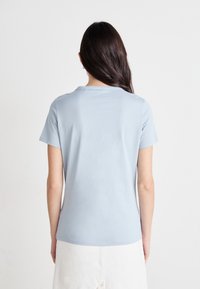 Light blue short-sleeve t-shirt with a round neckline; smooth texture and fitted design; seen from the back with minimal detailing.