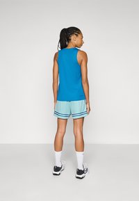 Sports tank top in blue, paired with mint green shorts featuring a textured pattern and blue stripes. Worn with black and white sneakers.