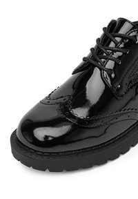 Czarne lakierowane buty skórzane z wytłoczonym wzorem, gładką fakturą, okrągłym noskiem i sznurowadłami, z grubą czarną podeszwą i dekoracyjnymi perforacjami.