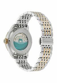 Reloj de acero inoxidable con una pulsera bicolor en plata y oro. Presenta un fondo transparente que muestra un mecanismo en tono aguamarina con detalles.