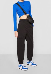 Niebieski prążkowany sweter cropped, czarne spodnie cargo z bocznymi kieszeniami oraz niebiesko-białe sneakersy z czarnymi akcentami. Mała czarna torebka crossbody.