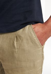 Khakifarbene Leinen-Shorts mit lockerer Passform, ausgestattet mit Seitentaschen und einem strukturierten Stoff. Kombiniert mit einem figurschmeichelnden T-Shirt in Marineblau.