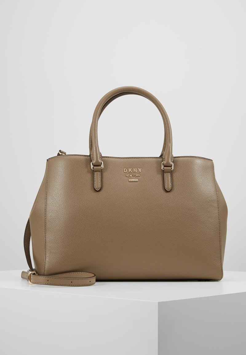 Sac à main DKNY en cuir taupe doux, doté de deux poignées supérieures, d'un logo doré en accent, et d'une bandoulière ajustable. Texture lisse.