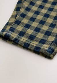 Zeleni in modri karo vzorec na tkanini, ki ima mehko teksturo in vidne šive ob robu. Vzorec izmenjuje kvadratke.