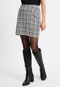 Schwarz-weißer karierten Minirock aus strukturiertem Stoff, kombiniert mit knieb hohen schwarzen Lederstiefeln mit Blockabsatz.