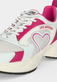 Λευκά και ροζ sneakers Love Moschino με σχέδιο καρδιάς, υφασμάτινο πλέγμα, λευκά κορδόνια και χοντρή σόλα.