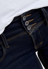Mörkblå denimjeans med hög midja, med tre metallknappar och kontrasterande gyllene sömmar längs kanterna.