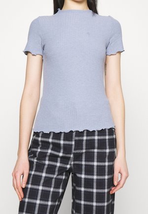 Haut à manches courtes en tricot côtelé bleu clair avec un col et un ourlet festonnés. Associé à un pantalon à carreaux noir et blanc avec un motif à damier.