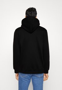 Černá mikina s kapucí a volným střihem, texturovaná látka a žebrované manžety. Spárovaná se světlými modrými džínami, představující ležérní outfit.