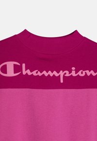 Felpa rosa in cotone con collo alto a girocollo. Presenta un grande logo "Champion" in rosa più chiaro sul petto. Gradiente di colore dal scuro al chiaro.