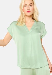 Light green satin top with a V-neck, short sleeves, and a relaxed fit. Features a smooth texture and subtle stitching details.