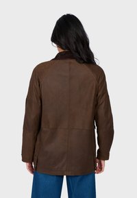 Brązowa skórzana kurtka z miękkim kołnierzem, rękawami raglanowymi i guzikami w bocznych rozporkach. Faktura z widocznymi szwami i luźny krój.