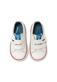 Zapatillas de lona blancas con suelas de goma rojas, dos correas de Velcro y plantillas azules con un gráfico de sol; diseño minimalista y práctico.