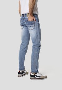 Lyseblå denimjeans med slim pasform, der har baglommer og kontrastsyninger. Kombineret med grå og hvide sportssko.
