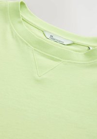 T-shirt en coton vert clair avec col rond, texture subtile et un petit point d'accent triangulaire au col.