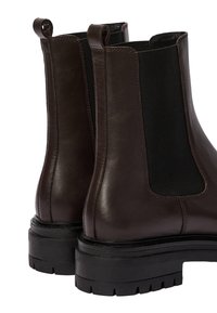 Bottines Chelsea en cuir marron avec des panneaux élastiques noirs, un bout arrondi et une semelle en caoutchouc noir épaisse. Tirants à l'arrière pour un enfilage facile.