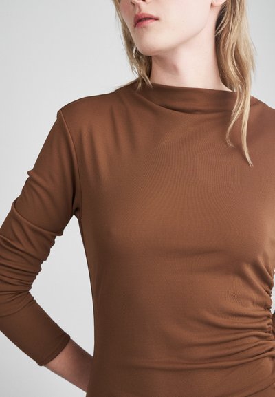 Brun langermet topp laget av glatt, elastisk stoff med høy hals og rysjer på siden, som fremhever en tett silhuett.