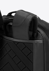 Sac à dos noir avec une surface texturée et un motif géométrique, doté d'une poignées rembourrée et de détails en maille. Fabriqué en tissu durable.