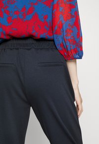 Röd och blå mönstrad blus med puffärmar, i kombination med marina byxor med platta bakfickor och elastisk midja.