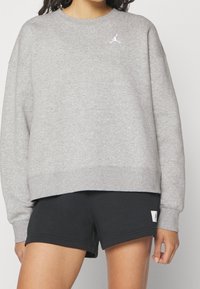 Sudadera gris con cuello redondo, hombros caídos y logo bordado en blanco. Combinada con pantalones cortos negros que tienen una etiqueta de logo. Tejido suave y casual.