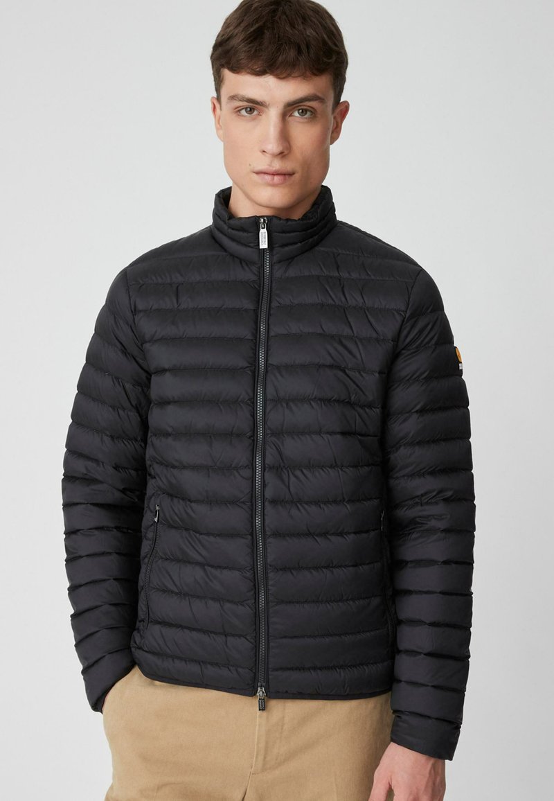 Giacca a sacco imbottita nera, trapuntata, con colletto alto, zip frontale e tasche laterali. Il design presenta cuciture orizzontali per l'isolamento.