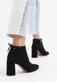 Stivaletti alla caviglia in suede nero con tacco a blocco, dotati di una cerniera laterale e un dettaglio a fiocco sulla parte posteriore. Design alla moda con punta appuntita.