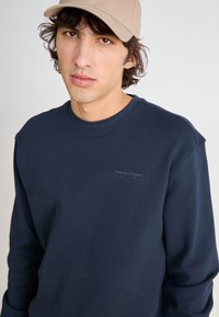 Sudadera de marina de manga larga, con cuello redondo y un sutil logo en el pecho. Tejido de mezcla de algodón suave con un corte relajado.