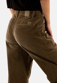 Pantaloni in velluto a coste marroni con vita alta, tasche laterali, tasca posteriore con un accento a forma di cuore e una finitura dalla texture liscia.