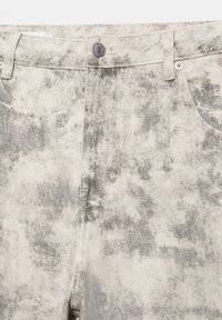 Gros plan sur le devant d'un jean taille haute avec fermeture par bouton et texture en denim gris et blanc délavé à l'acide.