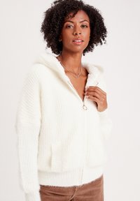Weiße Kapuzen-Zip-Up-Cardigan aus weichem, strukturiertem Strick mit geripptem Stoff, ausgestattet mit einem goldenen Reißverschluss und Fronttaschen.