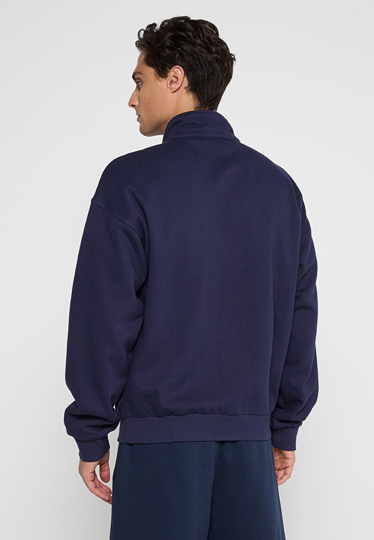 Felpa blu navy con colletto alto, spalle scese, polsini e fondo a costine; realizzata in materiale morbido con una texture liscia.