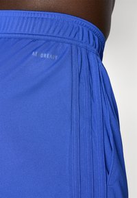 Modre atletske kratke hlače z teksturirano tkanino, elastičnim pasom in odsevnim logotipom "AEROREADY" na strani. Več nagub.