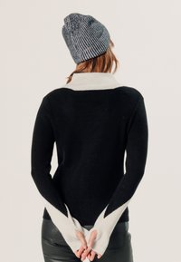 Zwarte trui met witte accenten, geribbelde mouwen met een chevronpatroon. Draag het met een grijze gebreide beanie. Zachte textuur en slim fit.