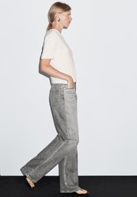 Gray denim jeans with a loose fit and straight legs, featuring two back pockets. Paired with a beige short-sleeve t-shirt.