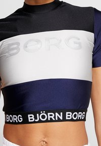 Cropped athletic top featuring a color-block design in black, white, and navy. Displays silver "BORG" lettering and a black branded waistband.