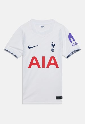 Biely futbalový dres Tottenham Hotspur s námorníckymi modrými logami na hrudi, červeným textom sponzora AIA a fialovým sponzorom Krait na pravom rukáve.