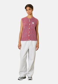 Červený a modrý textúrovaný pletený bezrukávový cardigan s okrúhlym golierom a predným gombíkovým zapínaním. V kombinácii so svetlošedými teplákmi a teniskami.