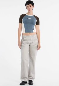 Cropped top met denim- en crèmepanelen, korte mouwen, voorzien van een logo. Lichtgrijze broek met wijde pijpen, eenvoudige ontwerp, gecombineerd met zwarte schoenen.
