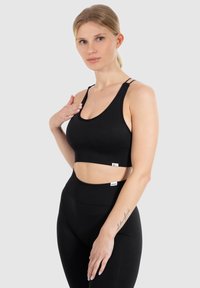 Svart kort sport-bh med racerback-design, justerbara remmar och mjukt tyg. Matchas med high-waisted svarta tights med logotypdetaljer.